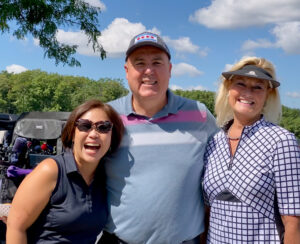 the three committee chairs from 2021 Conservation Corps laughing arm to arm with a blue sky and green golf course behind