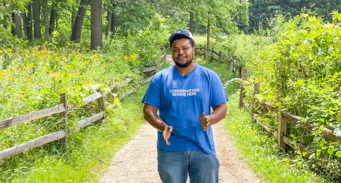 Young man in a blue shirt standing on a path surrounded by green forest preserves