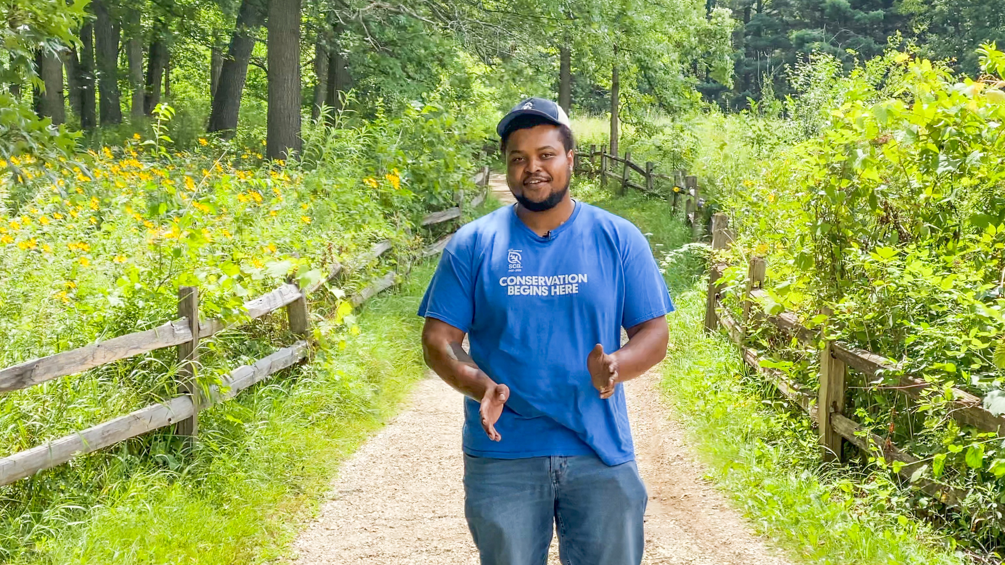 Young man in a blue shirt standing on a path surrounded by green forest preserves