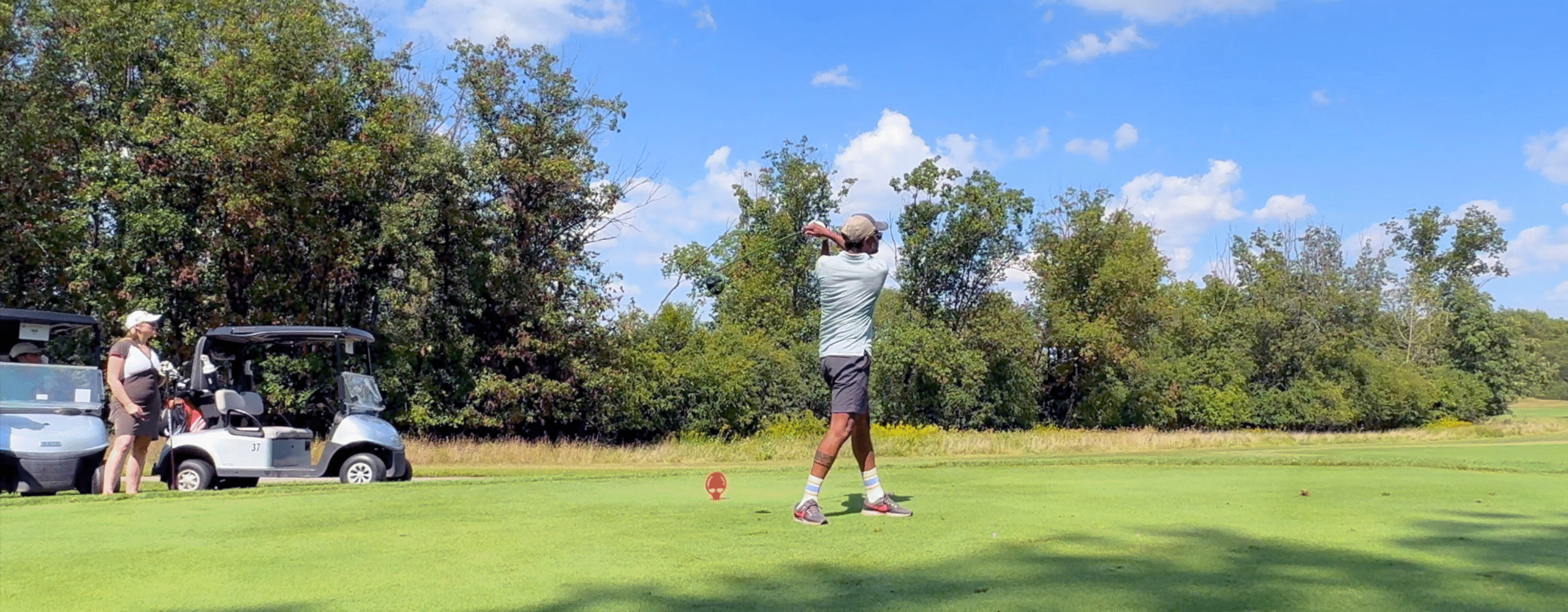 golfer swings with trees and blue sky in background